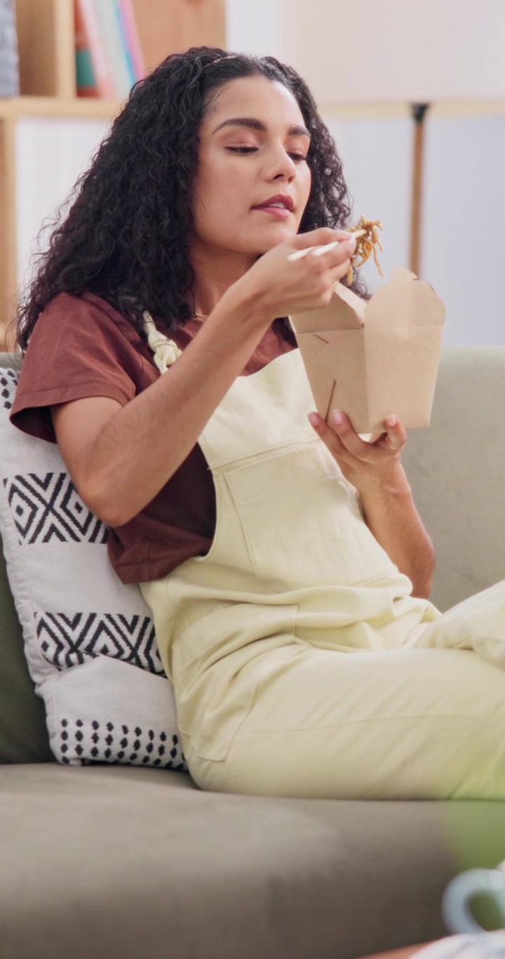 Giovane donna che mangia noodles da asporto sul divano