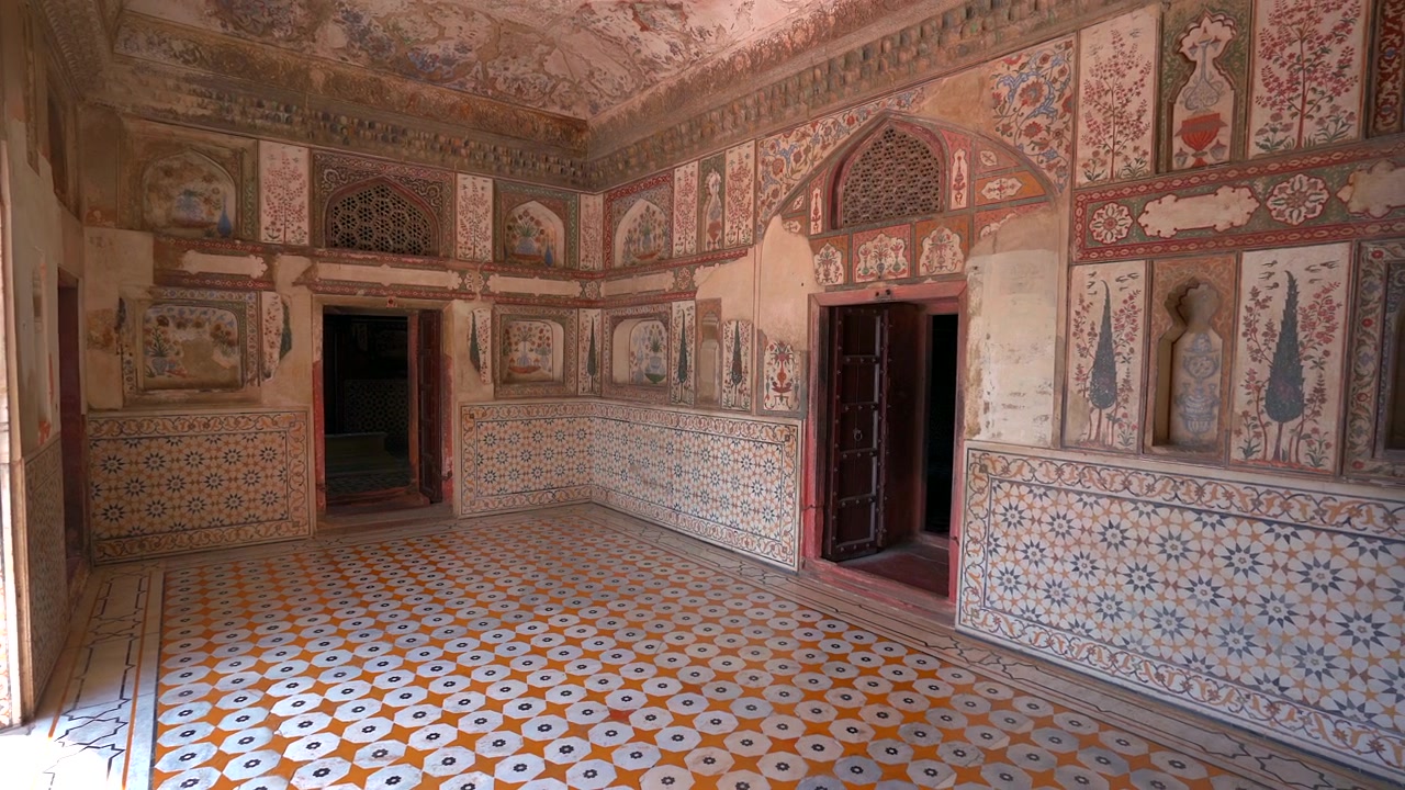 Una vista interna grandangolare della Tomba di Itimad-ud-Daulah, che mostra murales floreali finemente dipinti, pavimenti in piastrelle decorative e dettagli architettonici in stile persiano.