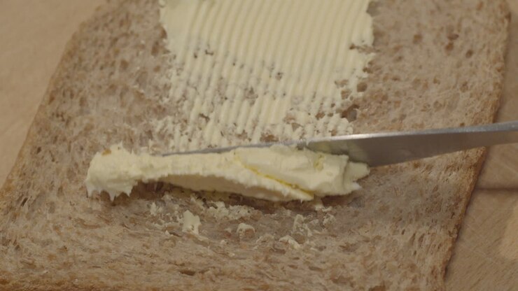 Margarine butter being spread on slice of whole grain bread