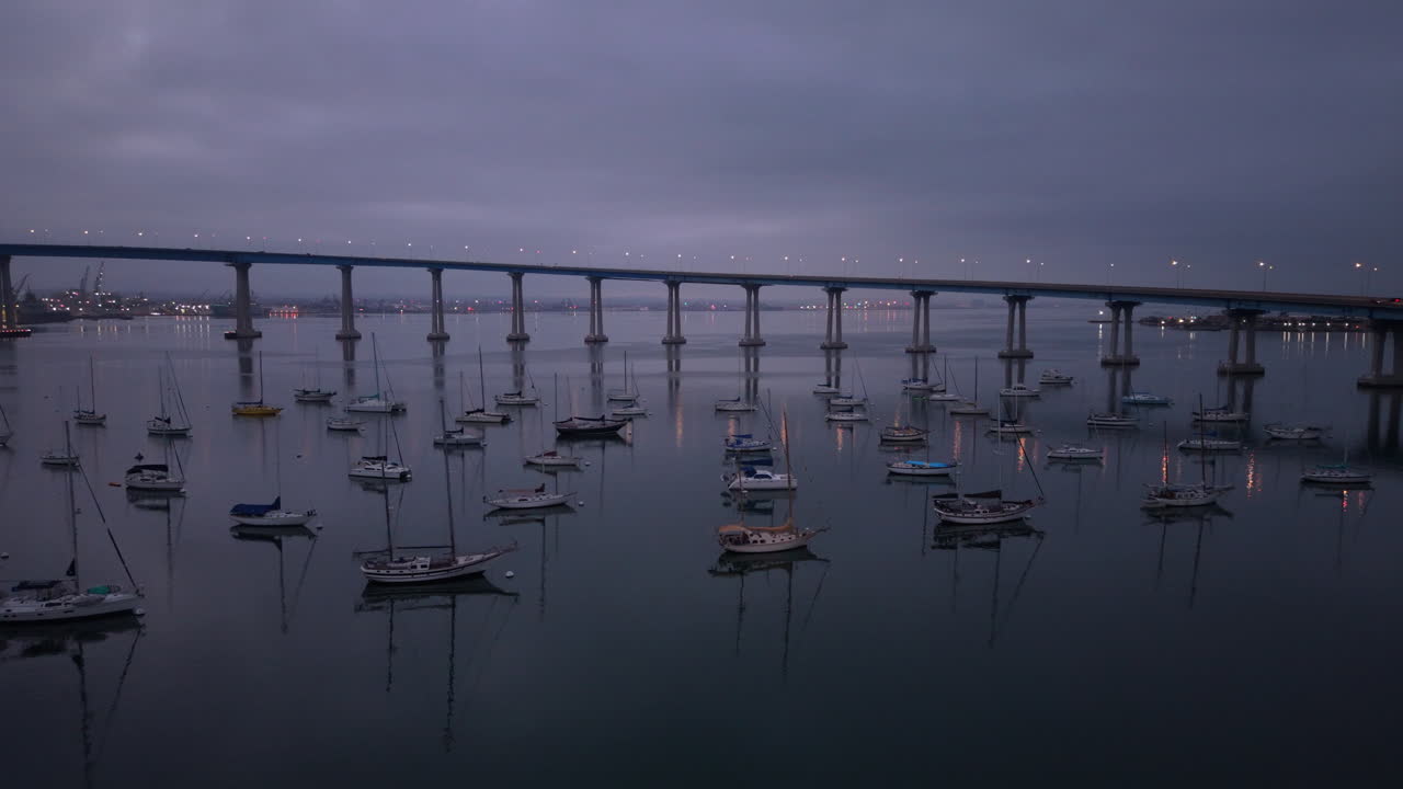 Early morning shot of the Coronado Bridge during moody blue hour lighting. Drone flying over boats and yachts