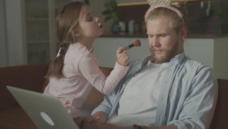 little daughter playing and making up man as princess, sitting on the sofa at home