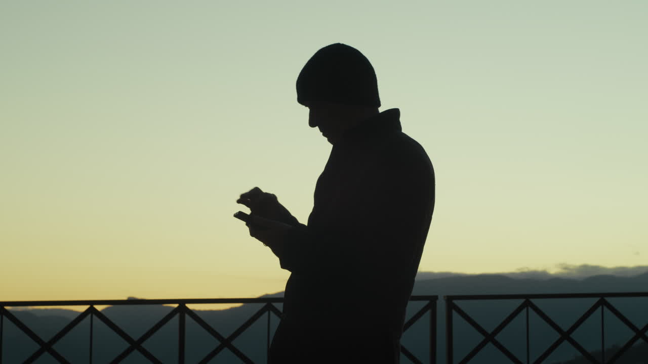 해가 지면 전화로 뉴스를 스크롤하는 남자의 실루