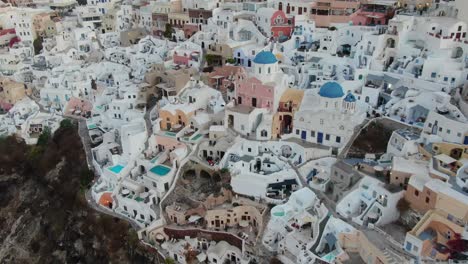 drone view in greece flying over santorini with oia town white houses and blue roofs on a cliff next to the mediterranean sea at sunrise