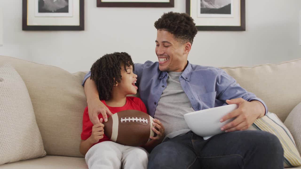 hombre biracial feliz y su hijo viendo un partido de fútbol americano juntos
