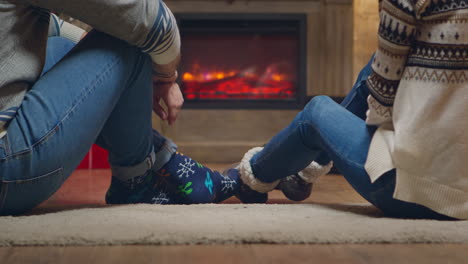 una pareja joven con calcetines cálidos frente a la chimenea.