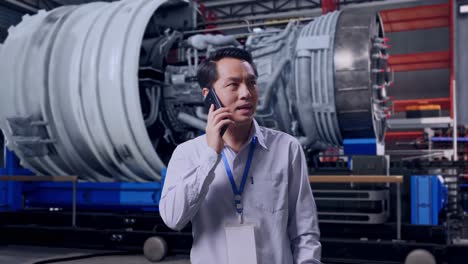 asian male professional worker standing with airplane engine maintenance conducted, analytics checking the turbine, he pick the phone up and started to speaking with it