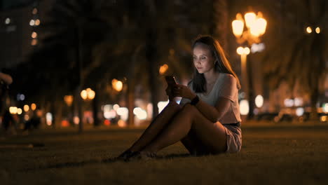 Young-woman-tourist-travels-through-the-night-megalopolis-and-writes-text-messages-on-social-networks-about-the-journey-holds-the-phone-in-her-hands-and-looks-at-the-screen-of-the-gadget