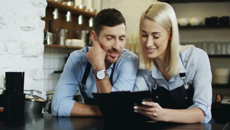 Young-Good-Looking-Waiter-And-Waitress-Standing-At-The-Bar-And-Making-Menu-Set,-Woman-Writing-With-Pencil