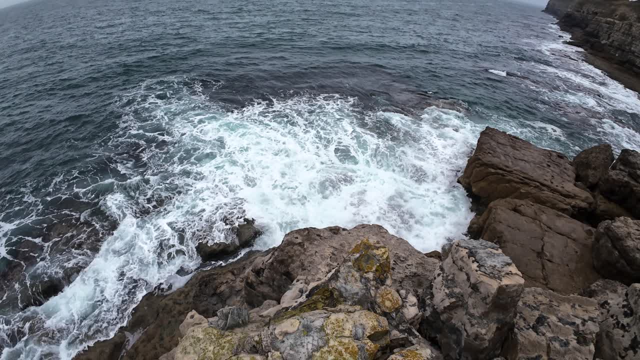 Dynamic aerial footage showcasing the rugged beauty of Dancing Ledge, Isle of Purbeck, Dorset. Waves crash against weathered rocks under overcast skies, moodily capturing natural coastal drama