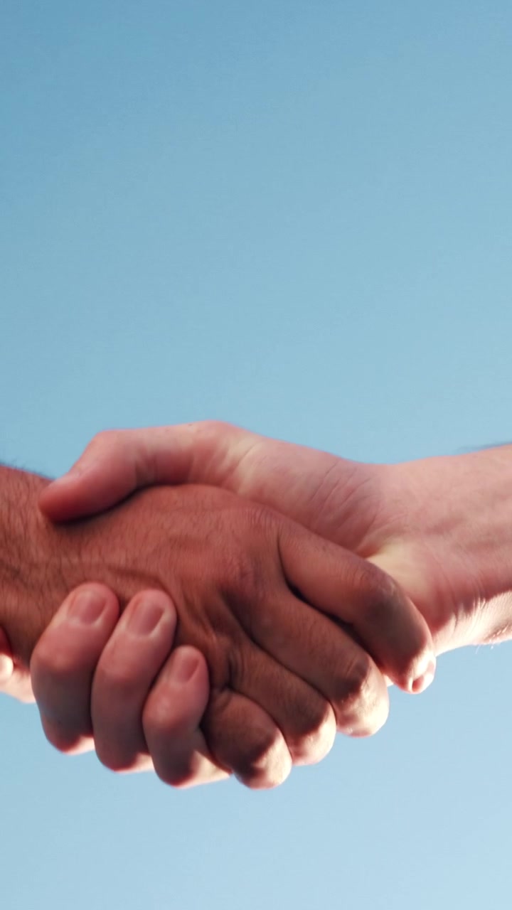 Two People Shaking Hands Against a Clear Blue Sky