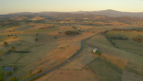 Dos-Automóviles-Viajando-A-Lo-Largo-De-Una-Vasta-Carretera-Rural-Durante-La-Majestuosa-Luz-Del-Atardecer-De-Otoño-En-El-Valle-De-Yarra,-Victoria,-Australia