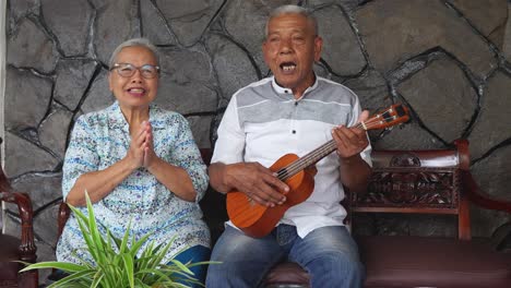 happy asian elderly couple with daughter playing ukulele guitar and singing together at home