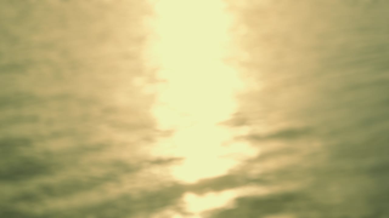 por el mar - pintoresco, hermoso bucle sin costuras de un tiro de 4k completamente desfocado de una superficie de agua ligeramente ondulada. el sol está bajo y la luz reflejada está brillando en la superficie del agua