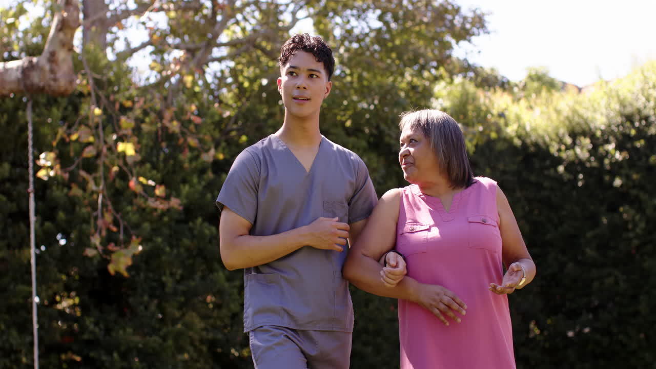 Caminando juntos en el jardín, fisioterapeuta masculino asistiendo a una mujer mayor