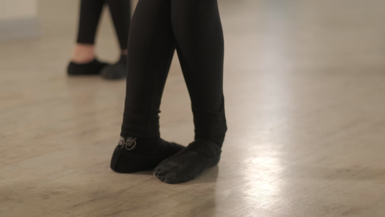 un grupo de jóvenes estudiantes de ballet con ropa de baile negra practicando posiciones en un amplio estudio de ballet con pisos de madera y barras montadas en la pared. expresiones enfocadas y movimientos sincronizados.