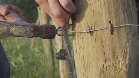 Macro Of A Farmer Pounding Metal Staples On Wire Fence Using A Hammer Inside The Ranch