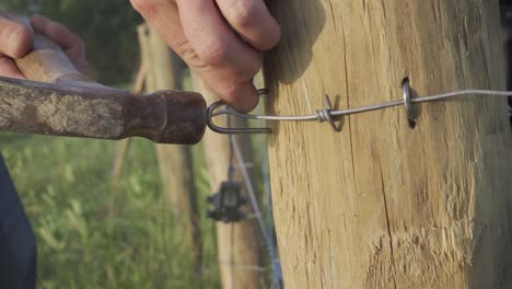 macro of a farmer pounding metal staples on wire fence using a hammer inside the ranch