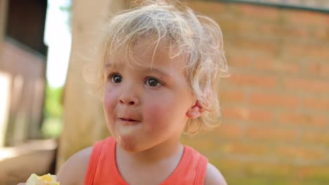 candid portrait of infant toddler eating an orange while outside in the sunlight. child eating healthy fruit outdoors in 4k