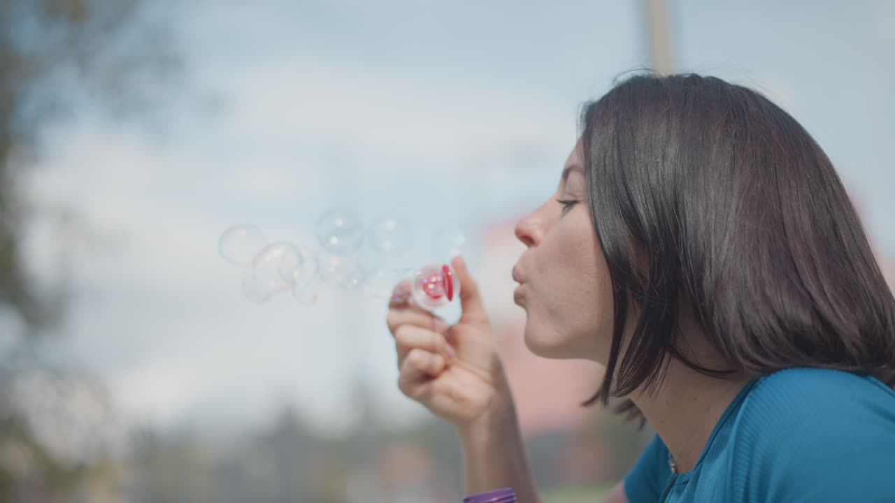 Parkside caucasian woman blowing bubbles, contemplative outdoor portrait with gentle sunlight, sideprofile shots show slow breaths, playful attempts, subtle smiles narrative frames suggest