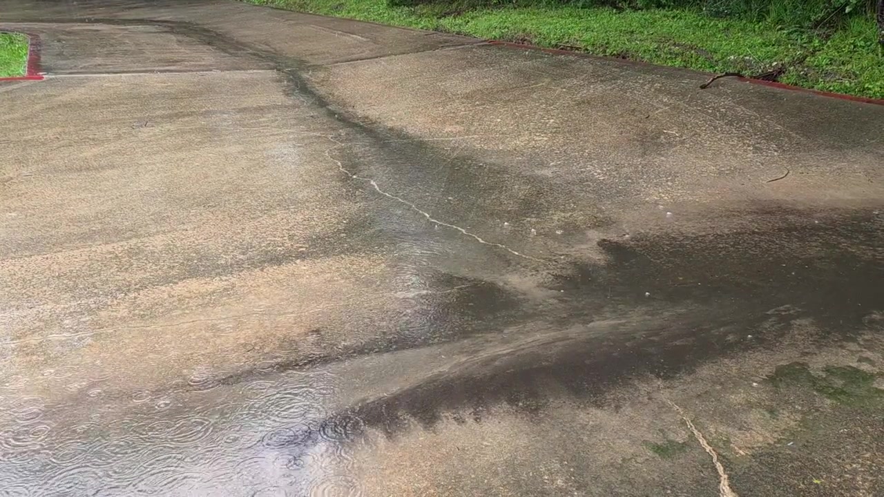 Una pioggia leggera cade su vecchio cemento con l'acqua che defluisce nell'erba circostante.