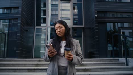 low angle view of business chinese woman standing on the street in the city and texting phone