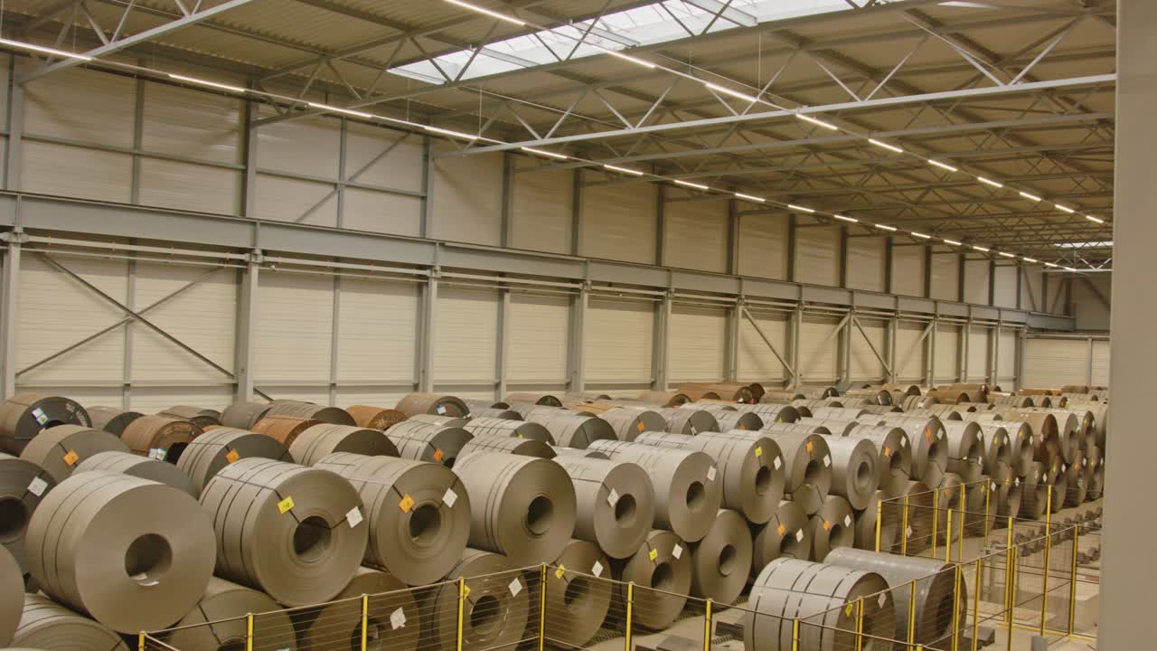 Panorámica amplia de un gran almacén lleno de grandes bobinas de acero en fleje.