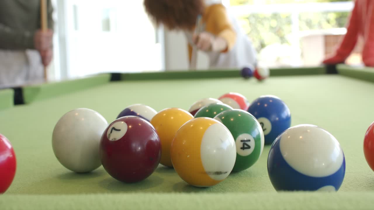 Woman placing cue ball, delivering break shot to scatter balls on pool table while friends watch