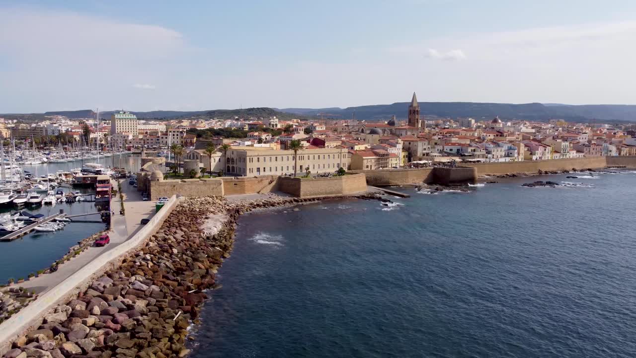 Lenta ripresa cinematografica con drone del centro storico di Alghero in Sardegna, Italia, con un grande porto turistico e yacht di lusso in primo piano