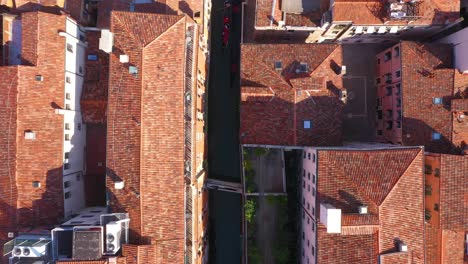 Statische-Luftaufnahme-Von-Oben-Nach-Unten-über-Den-Kanal-Und-Die-Dächer,-Während-Die-Gondel-An-Einem-Sonnigen-Tag-In-Venedig-In-Italien-In-4k-Vorbeifährt