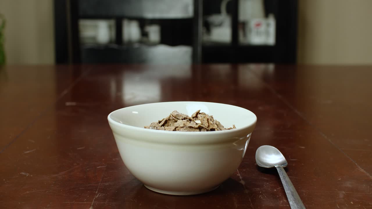 Cereali versati da una busta di plastica in una ciotola bianca su un tavolo.