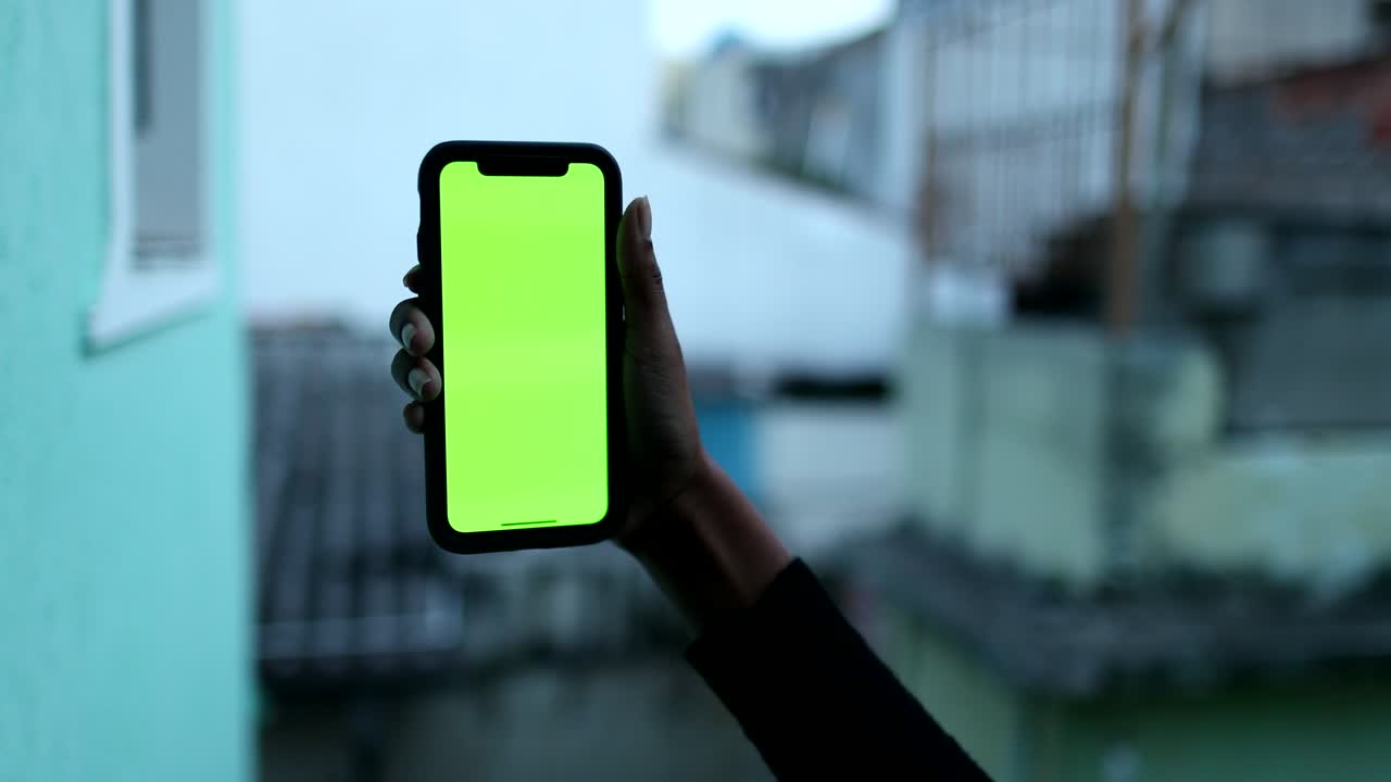 mano femenina negra sosteniendo un teléfono móvil con una maqueta de pantalla verde