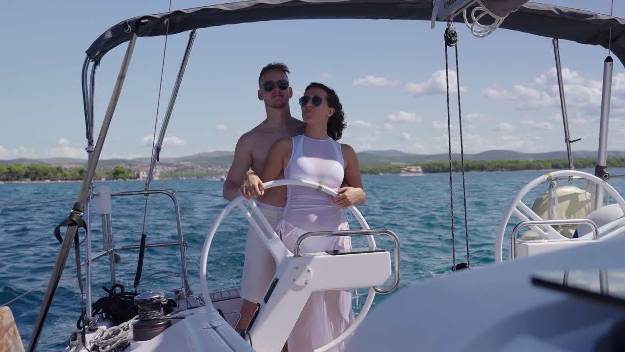 Majestic couple in white clothes stand behind rudder on modern yacht, front view