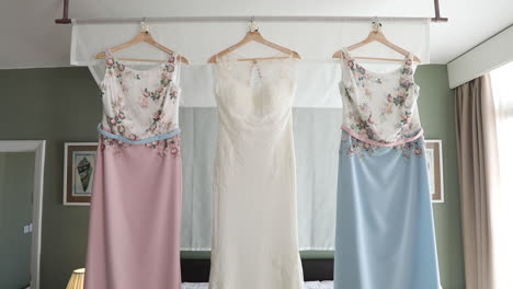 three beautiful dresses hanging over a bed belonging to a bride and her bridesmaids