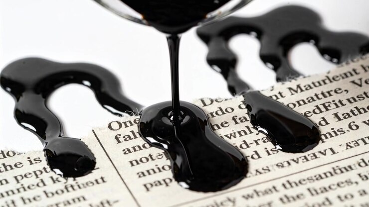 Pouring thick black liquid flowing from rim, forming glossy pools obscuring newspaper text on table