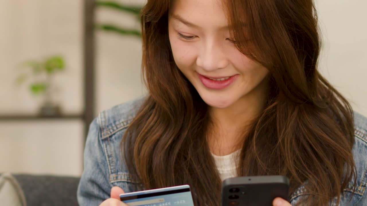 クレジットカードを持ちながら、スマートフォンで支払い情報を入力する幸せそうな若い女性
