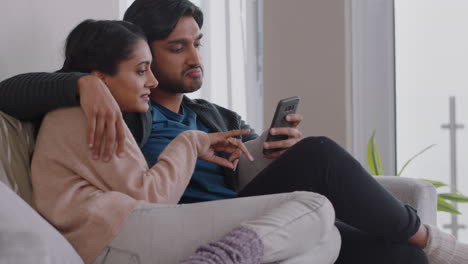 happy couple relaxing at home using smartphone together shopping online enjoying browsing internet relaxing on couch