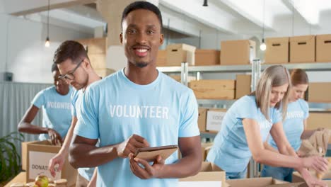 voluntario afroamericano escribiendo en una tableta y sonriendo a la cámara