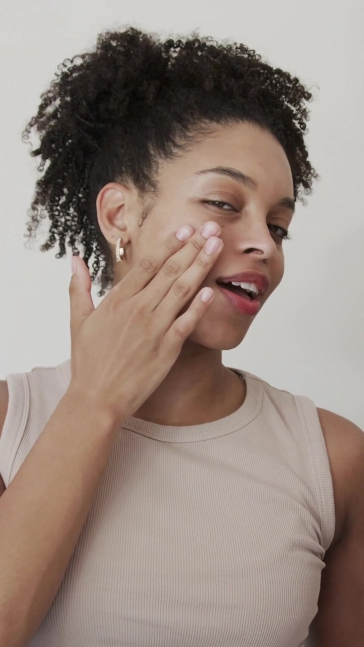 Vertical video: Dabbing cream to cheek, tan tank woman dipping from jar blending at home hydrating