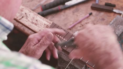Die-Hände-Eines-Geigenbauers-Installieren-Bünde-Auf-Dem-Griffbrett-Einer-Gitarre---Nahaufnahme