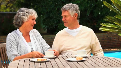 Mature-couple-sitting-in-the-garden-having-tea-and-cake