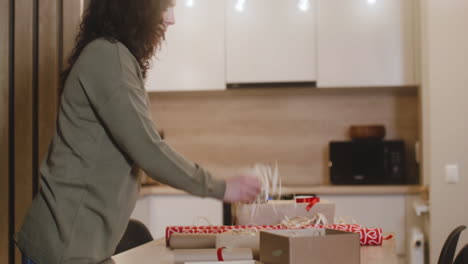 side view of brunette woman wrapping christmas presents on a table in a room decorated with a christmas tree