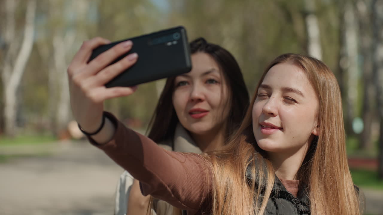 amigos haciéndose selfies alegres, amigos jóvenes haciéndose selfies espontáneos al aire libre, foto informal y animada al aire libre de dos amigos mostrando actitudes juguetonas bajo el sol de la primavera