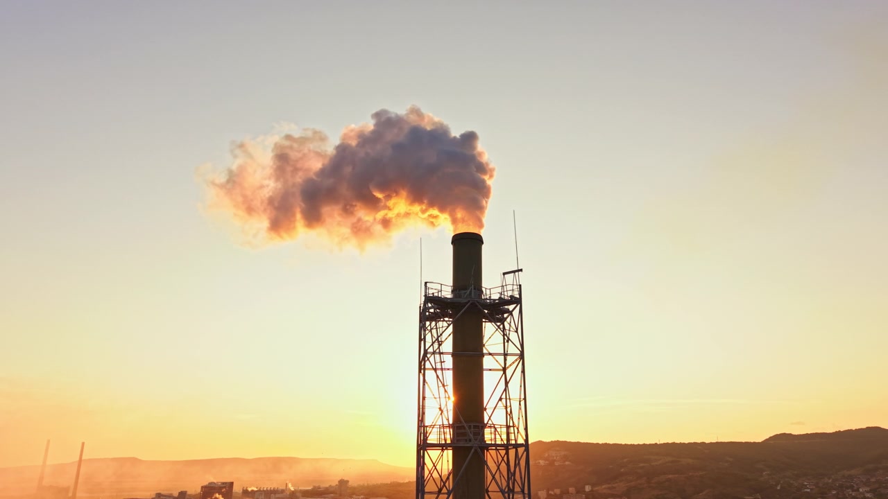 Ciminiera di fabbrica rilascia vapore al tramonto su un'area di produzione