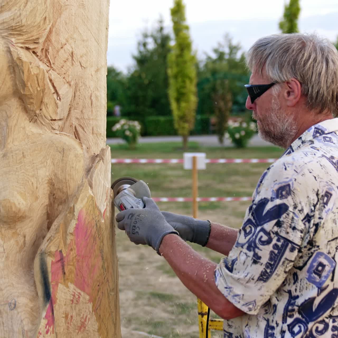 Creative process of a female sculpture making. Grey-haired man uses electric tool to cut wood