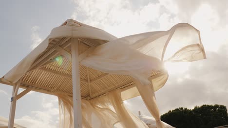 una tormenta inminente en el balneario. un viento fuerte desarrolla una tela de dosel blanco en la cama de sol de la playa en el resort. video 4k