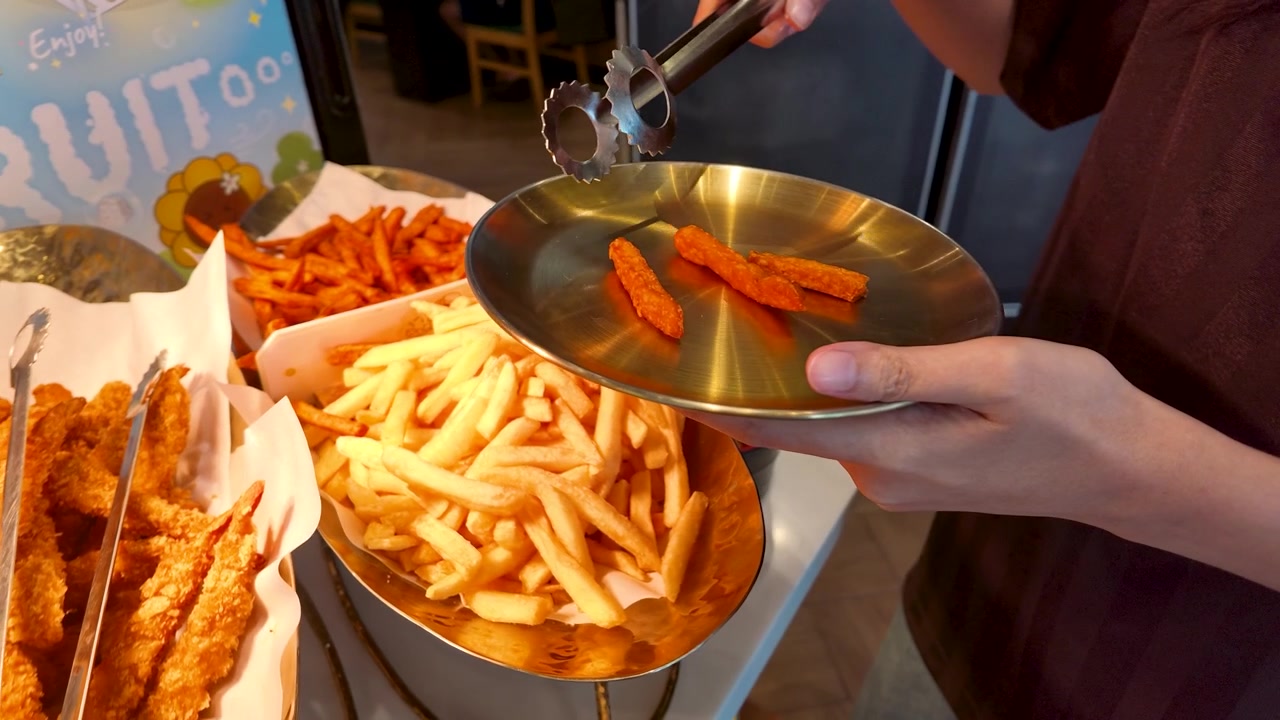 Close-up shot of hands using metal tongs to place fried snacks onto a gold plate.