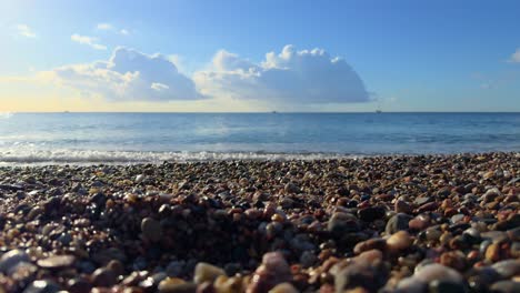 Sandstrand-Und-Kleine-Steine-In-Zeitlupe-Mit-Kleinen-Wellen,-Blauem-Himmel