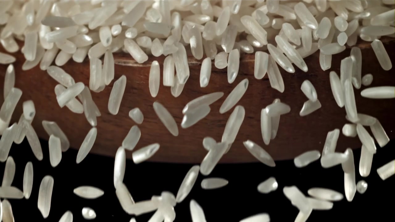 Movimento rallentato di chicchi di riso bianco che cadono su uno sfondo nero