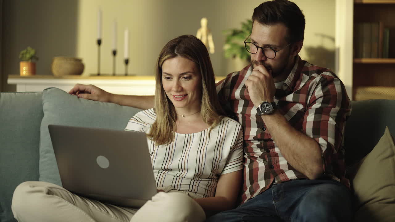 una pareja usando una computadora portátil en el sofá.