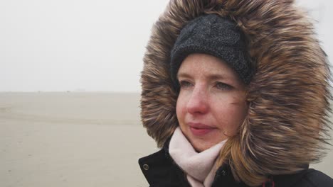 Young-woman-with-a-fur-hood-facing-strong-wind-in-freezing-cold-landscape---Slow-Motion